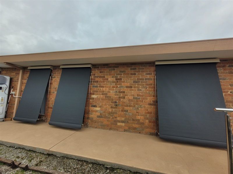 Charcoal drop arm awnings on brick-home windows