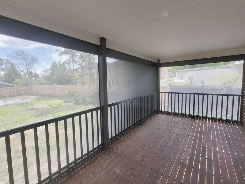 Covered timber deck with mesh outdoor blinds lowered between the posts, looking out to a leafy backyard