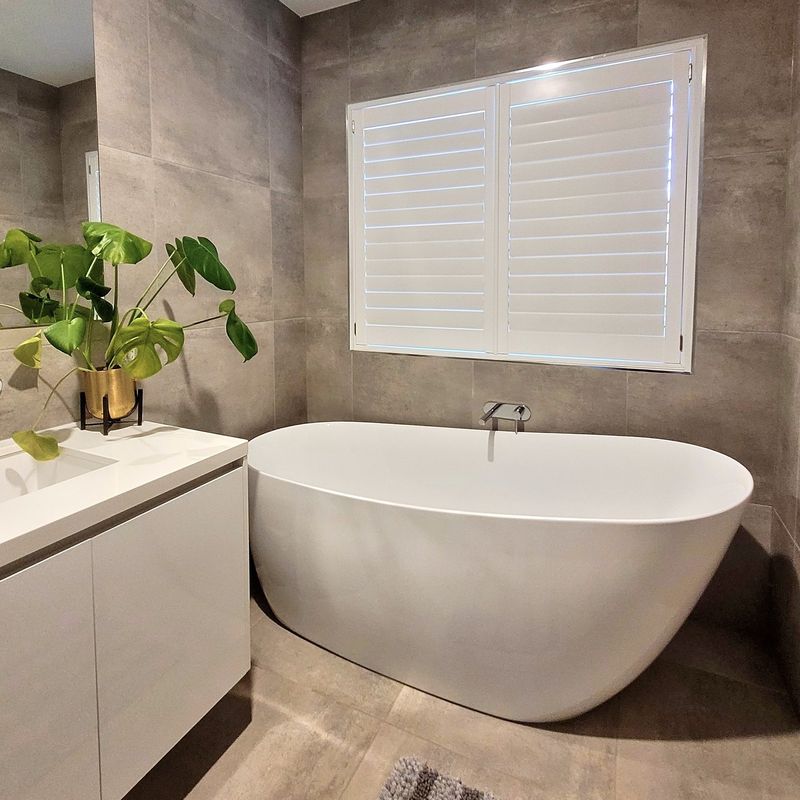 Plantation shutter above a freestanding bath in a tiled bathroom in Cowes