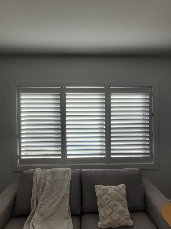 White plantation shutters on a living room window with a grey armchair